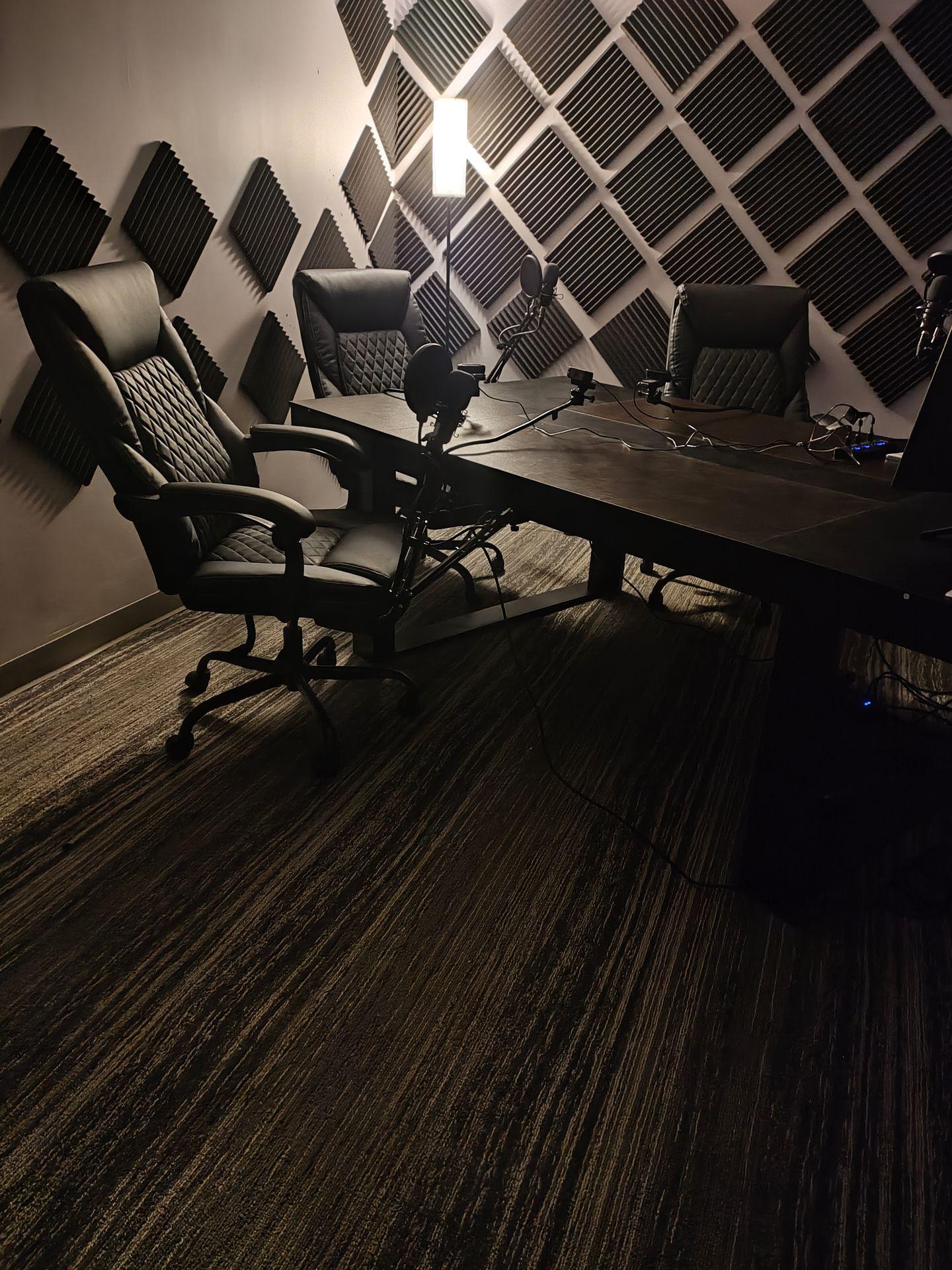 Modern podcast studio with black chairs, microphones, and soundproofing foam panels on walls.