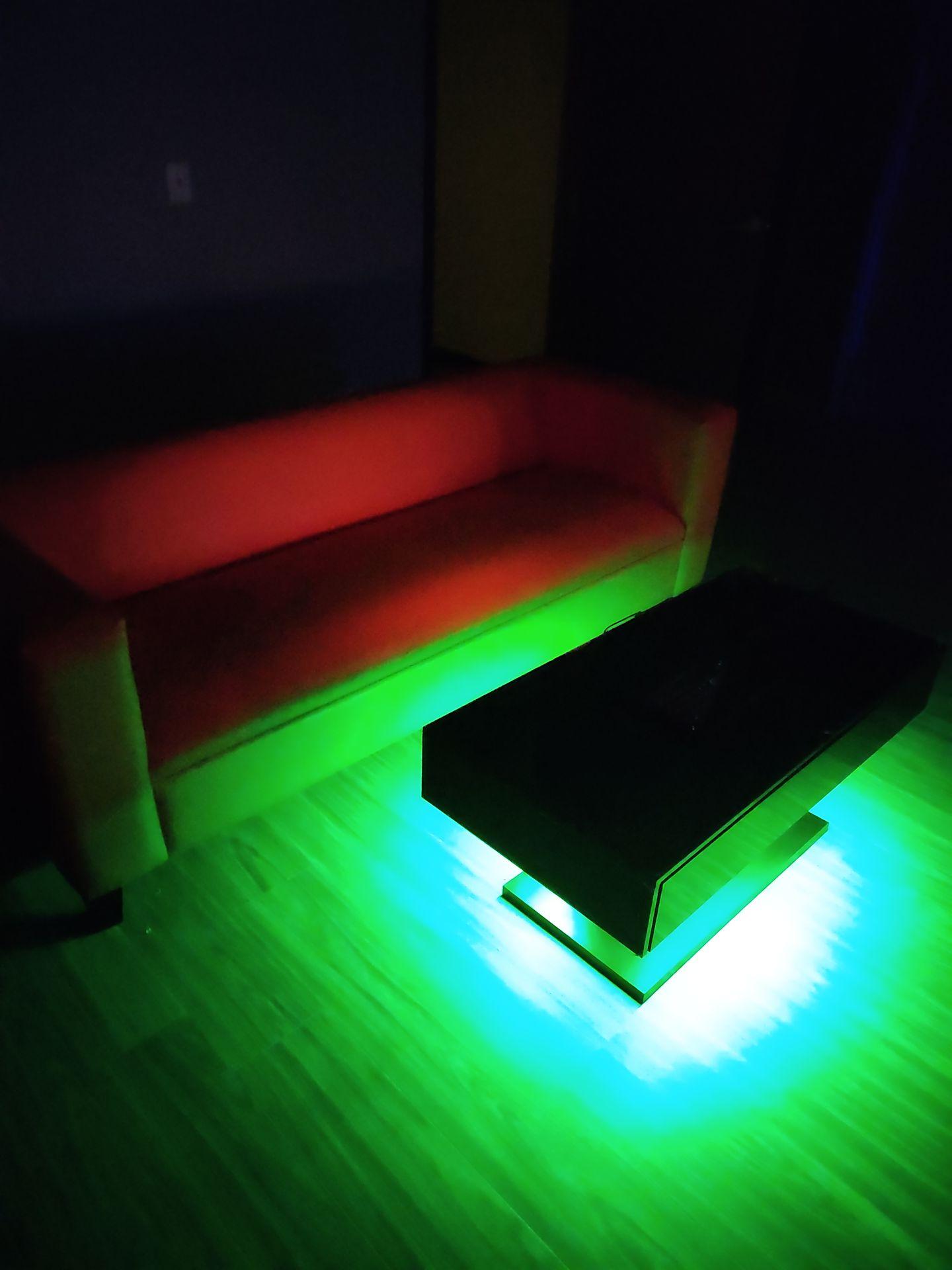 A dark room with a red sofa and a black table illuminated by green lighting on the floor.