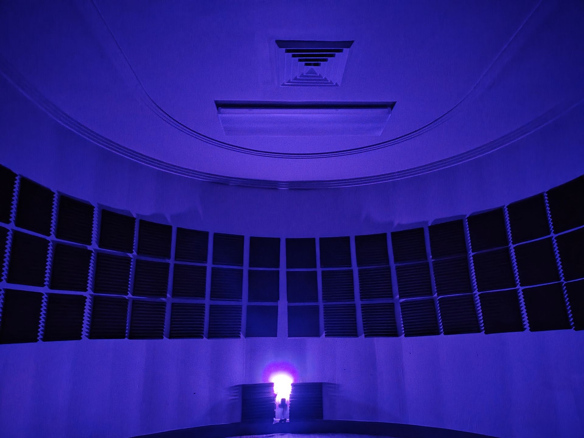 Dark room with acoustic foam panels on walls, illuminated by a blue and pink light.